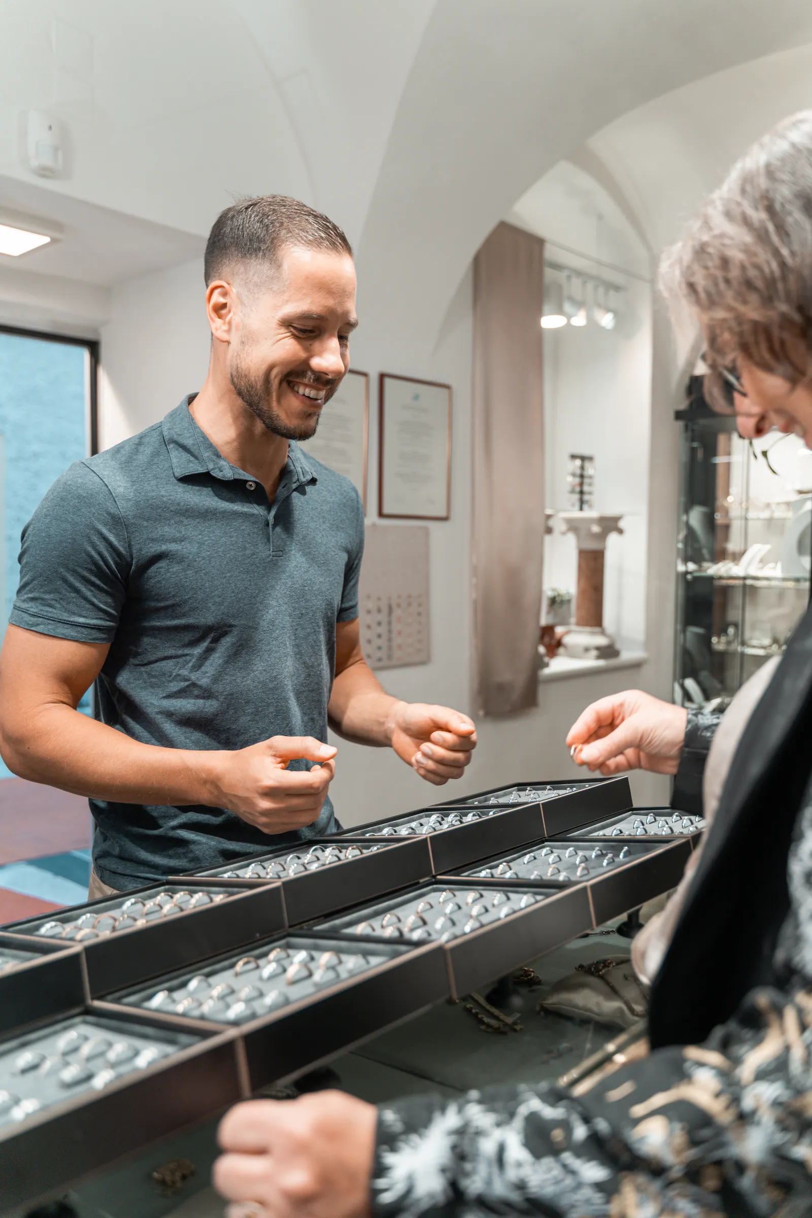 Ein Kunde wählt lachend Ringe an der Vitrine aus