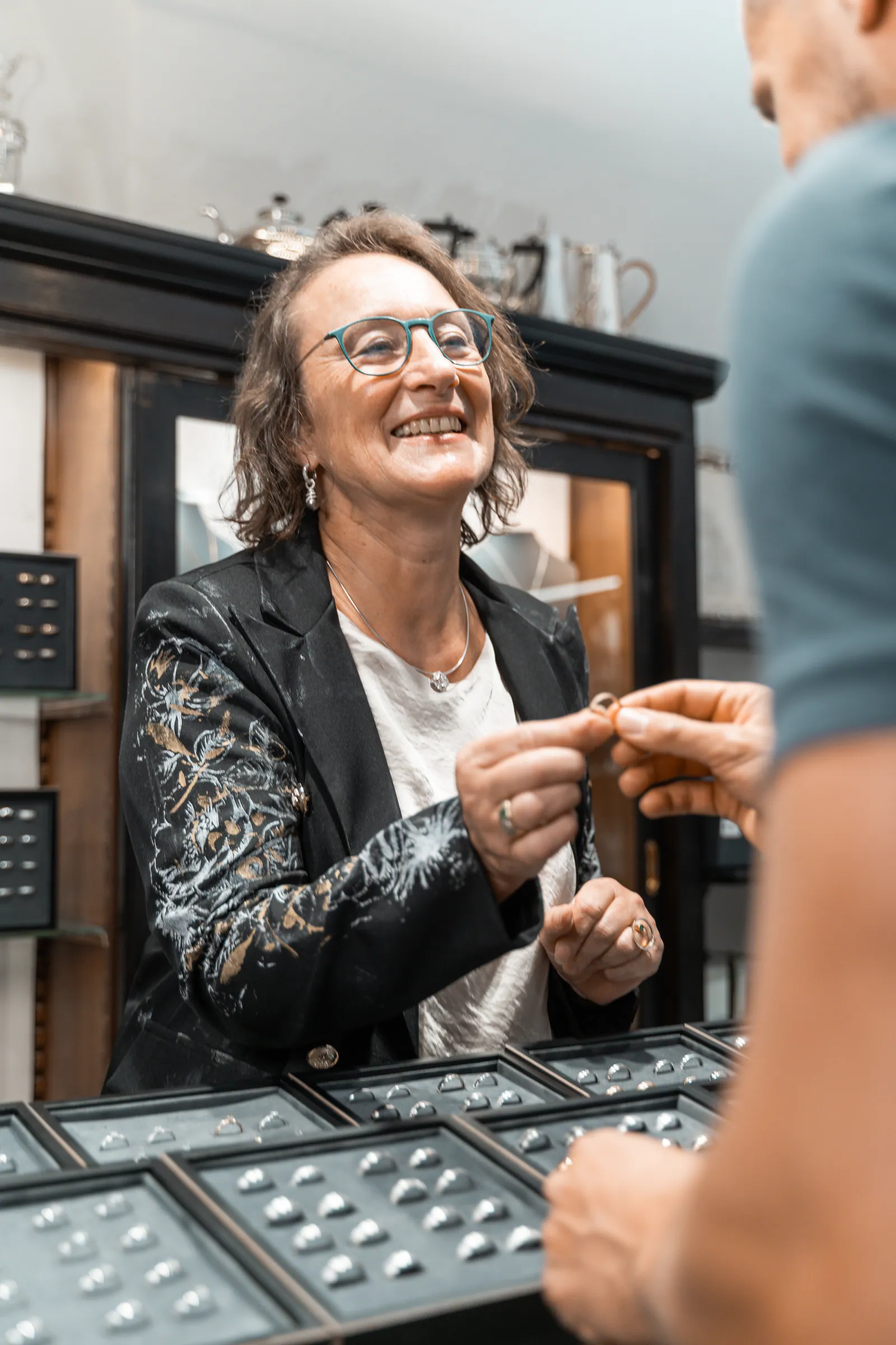 Frau Winkler reicht einem Kunden lachend einen Ring über die Vitrine